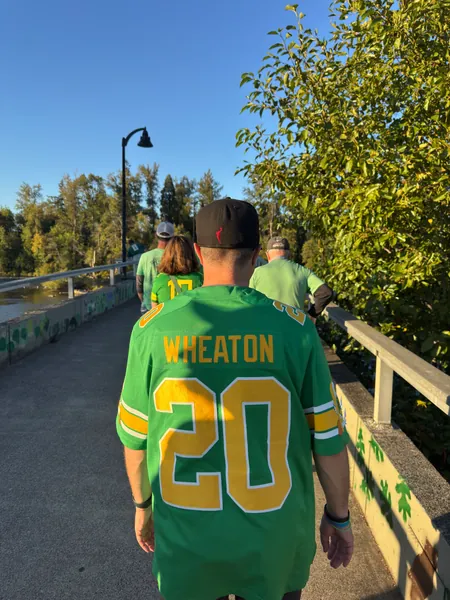A guest in an Oregon jersey walks across a pedestrian bridge.