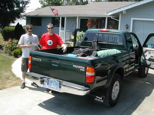 Travelers stand beside a pickup loaded beneath a blue tarp.