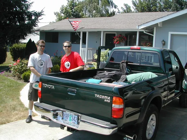 Two travelers beside a pickup truck packed for a summer road trip.