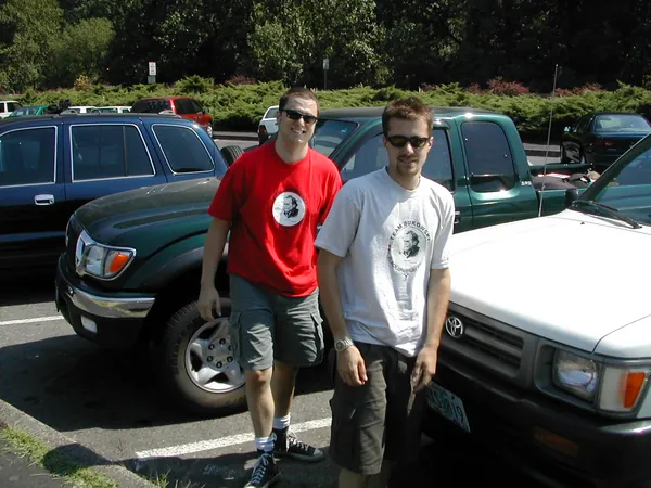 Two travelers stand beside parked sport utility vehicles.