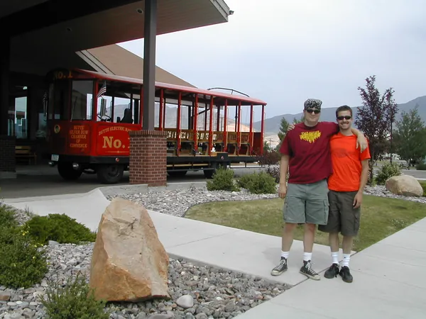 Two travelers pose beside a red trolley.