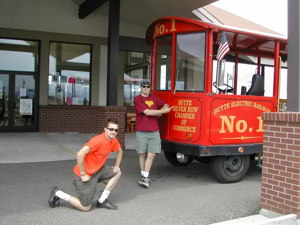 One traveler sits while another stands beside the trolley.