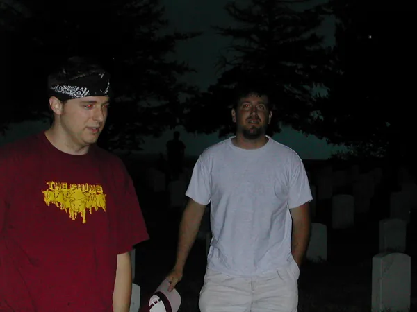 Two travelers stand among the cemetery markers.