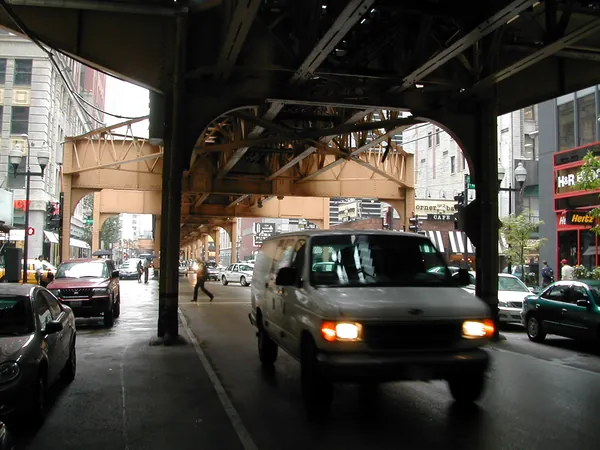 Vehicles and storefronts under the tracks.