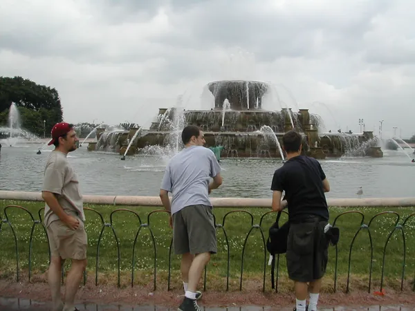 Three travelers stand at the edge of a large fountain.