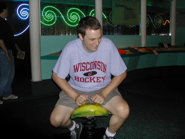A traveler sits on a brightly lit arcade ride.
