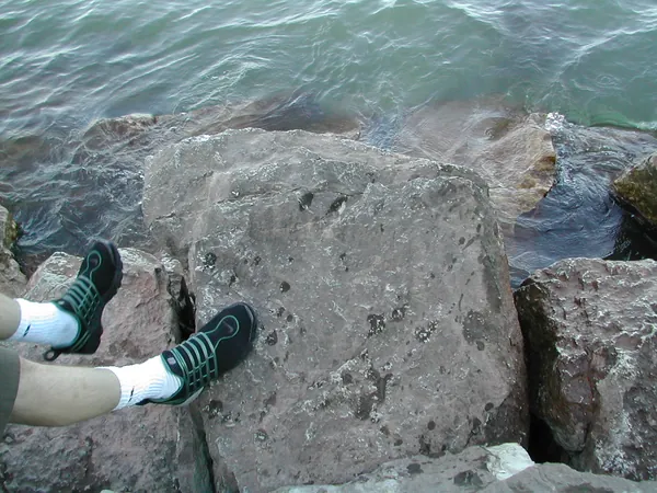 Two pairs of shoes rest on lakefront rocks.
