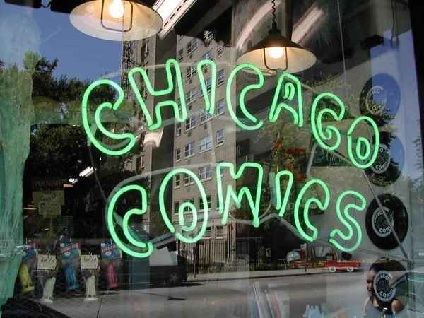 A neon Chicago Comics sign in a storefront window.