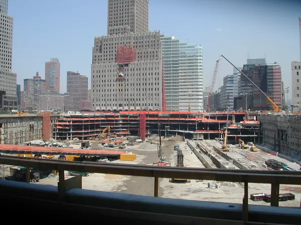 Steel, cranes, and nearby buildings beyond the fence.